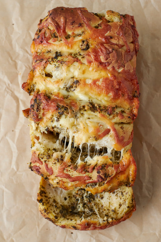 Loaf of bread with cheese and herbs on a crumpled brown parchment paper.