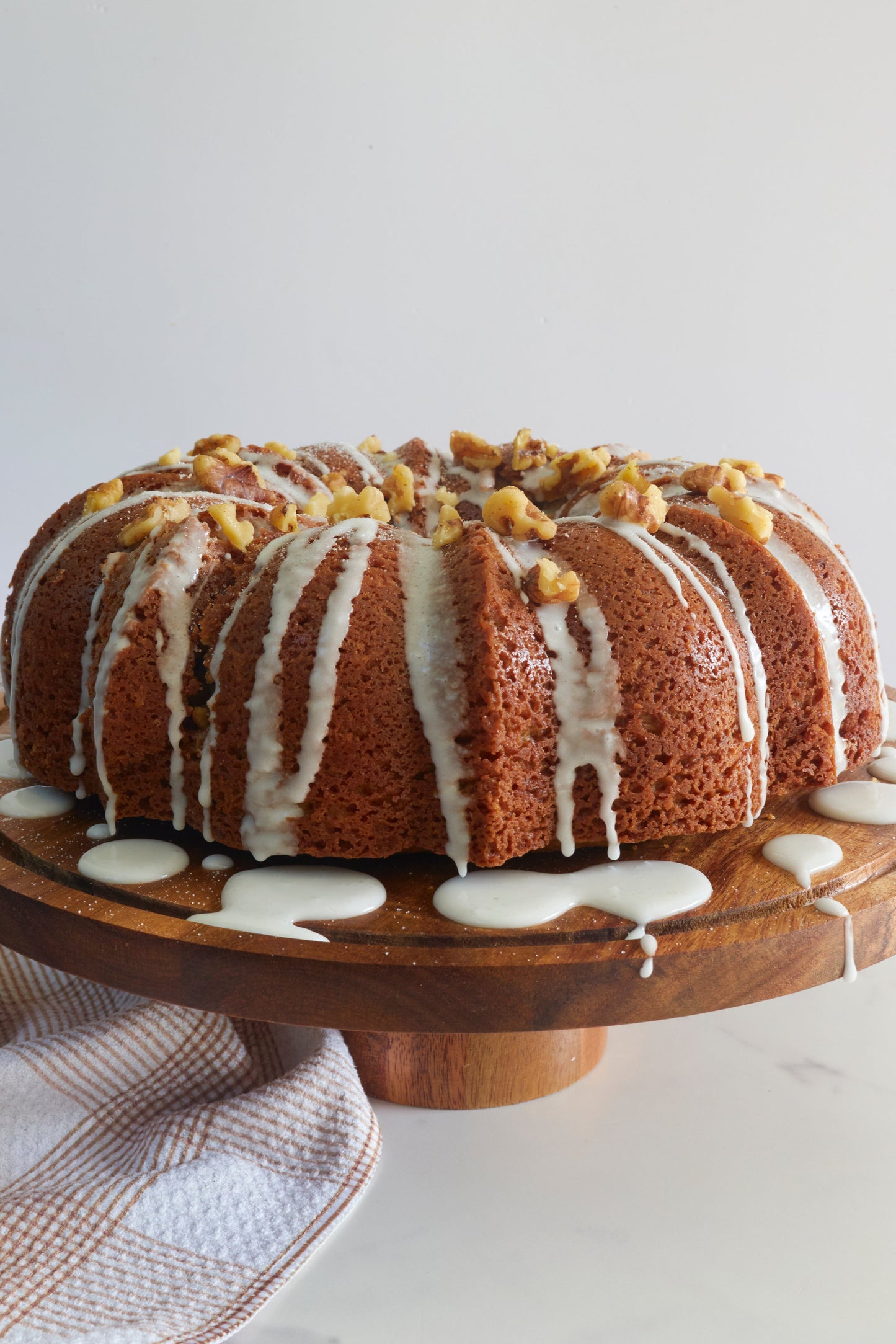 Sourdough bundt cake with white icing on a wooden stand against a white background from Same Day Sourdough cookbook. 